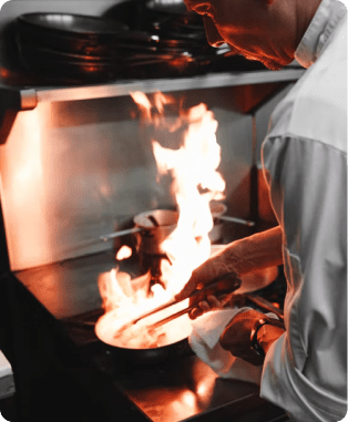 A Chef flambaying a in a frying pan on a stove