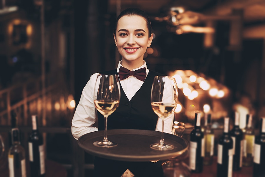 A waitress holding a tray with glasses of white wine and do