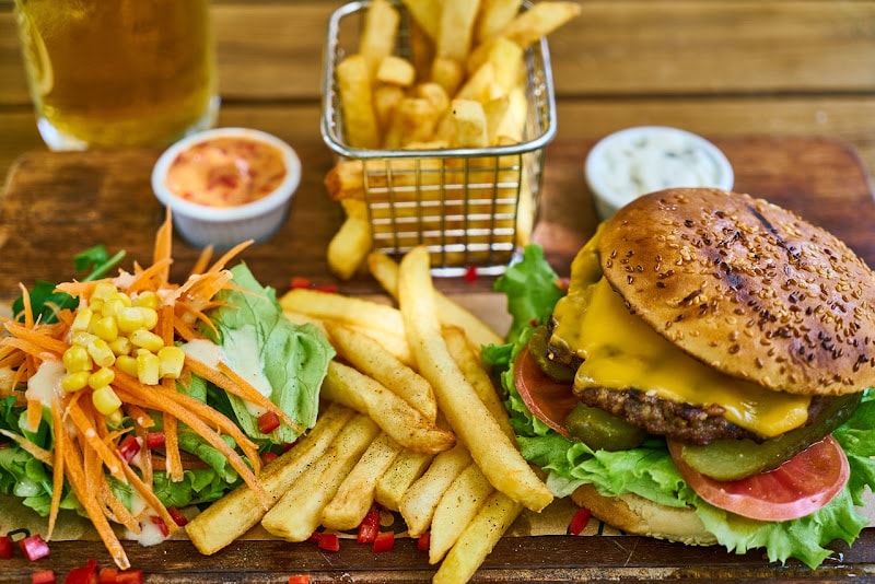 Cheeseburger, fries, beer and dipping sauces with a small side salad of some lettuce, corn and carrots