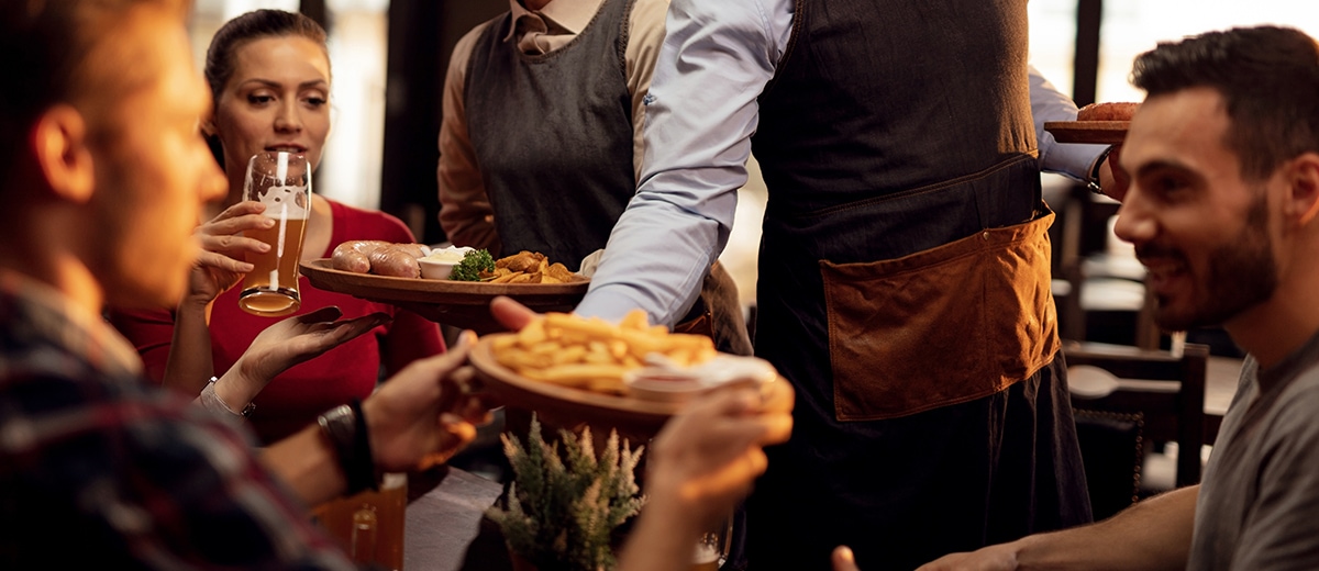 Waiter and waitress serving fries and a meal to happy customers drinking beer.