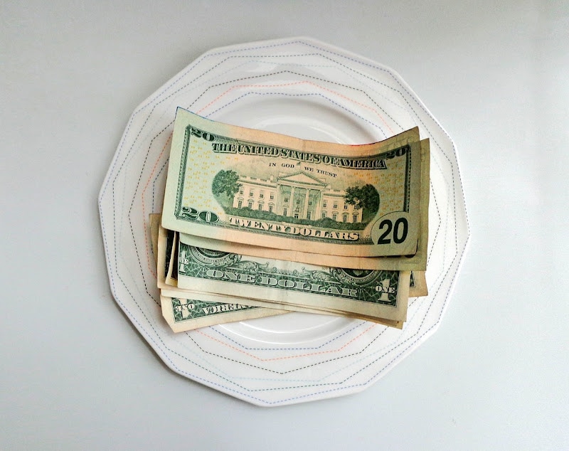 Cash payment with twenty dollars and single dollars on a plate.